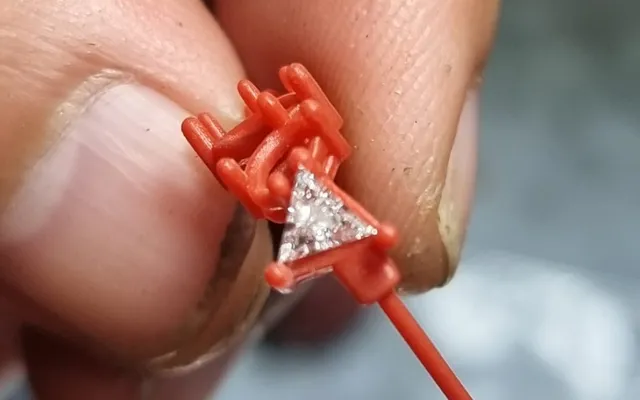 3D-printed resin model of a ring head with a triangle diamond set in place, held between two fingers