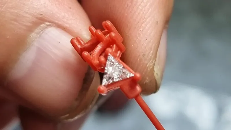 3D-printed resin model of a ring head with a triangle diamond set in place, held between two fingers